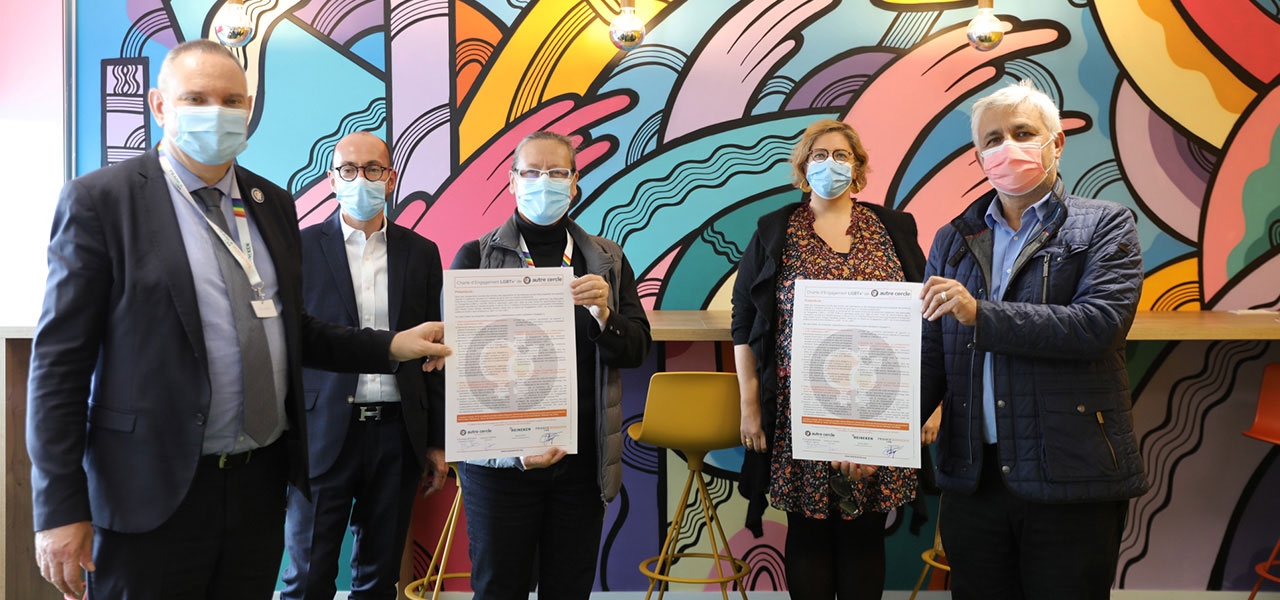 Quatre personnes masquées tenant des documents devant une fresque murale colorée lors d'une rencontre officielle.