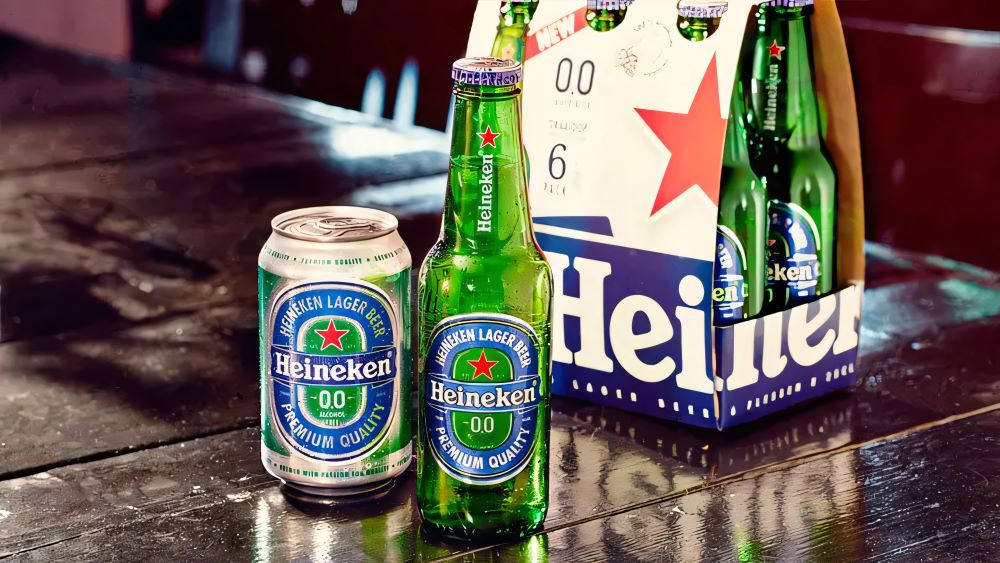 Pack de bières Heineken 0.0% avec une bouteille et une canette sur une table, et un pack de six en arrière-plan.