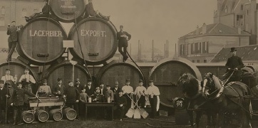 Photographie vintage en noir et blanc montrant des ouvriers devant de grandes barriques de bière marquées 'Lagerbier Export', représentant une ancienne brasserie.